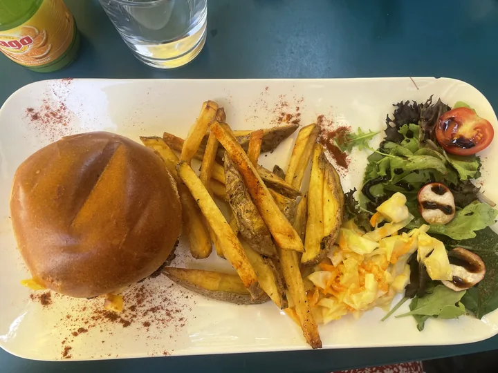 Burger, frites épicées et salade verte servis sur une planche blanche