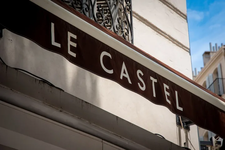 Le store brun de la brasserie, avec « LE CASTEL » en lettres blanches, sous un balcon en fer forgé