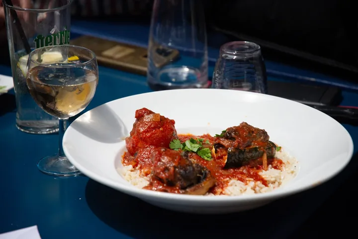 Assiette creuse d'un plat en sauce tomate sur du riz, avec un verre de vin blanc